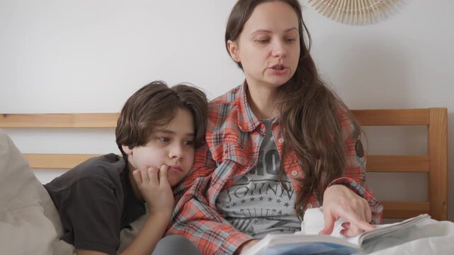 Mother reads aloud to her child, helping him practice and improve his literacy skills. Parent and son follow the text in a book together, developing fluency and correct pronunciation at home.