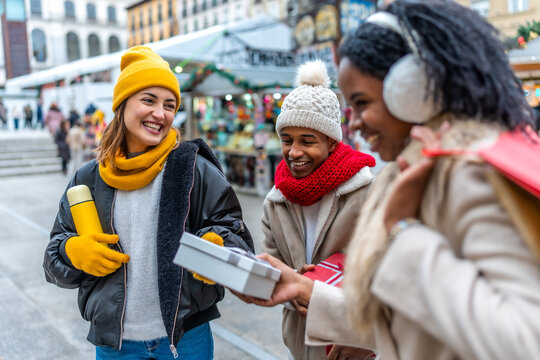 Happy multi ethnic friends exchanging christmas gifts at a winter street market - Powered by Adobe