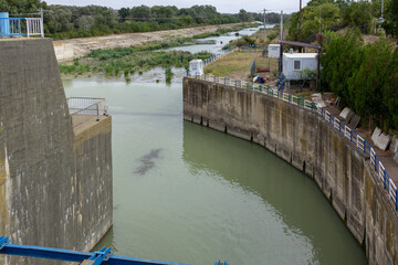 Industrial water dam and canal infrastructure with flowing river and concrete barriers under a cloudy sky