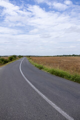 Asphalt road curving through rural fields under a partly cloudy sky