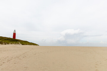 Red lighthouse stands tall on sandy beach with expansive sky and gentle waves creating a serene coastal atmosphere. Texel lighthouse. free space