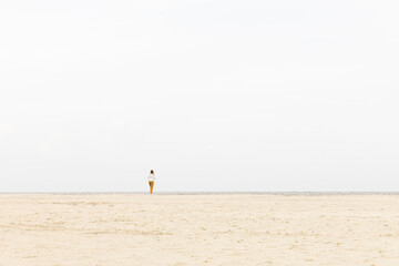Man standing alone on a wide sandy beach, surrounded by vast open space and soft natural light, evoking a sense of solitude and tranquility
