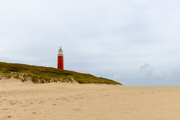 Red lighthouse stands tall on sandy beach surrounded by green grass under a cloudy sky with serene atmosphere. Texel lighthouse. free space