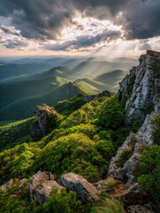 Dramatic sunlight piercing through clouds over lush green mountain ridges and rugged rocky cliffs creating a breathtaking panoramic natural landscape scene