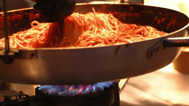 Italian cuisine. A large aluminum pot filled with deep orange pasta and sauce hangs over a blue gas flame. Street food and outdoor cooking. Italian cuisine, culinary events.