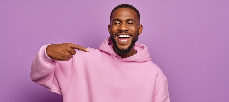 Cheerful young man in pink hoodie pointing at himself and smiling on purple background, symbolizing confidence, self promotion, positivity, and modern youth lifestyle.