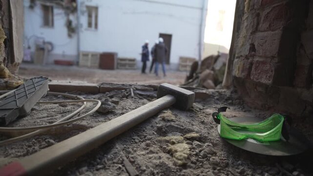 Piles of sand broken concrete and tools rest near building exit. Heavy sand along with concrete fragments cover ground near doorway