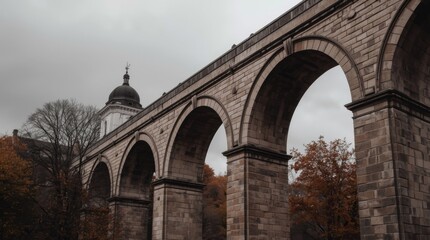 A majestic stone viaduct arches over a tranquil autumn landscape under a cloudy sky