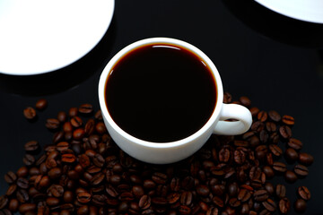Black coffee cup with coffee beans closeup shot on black background 