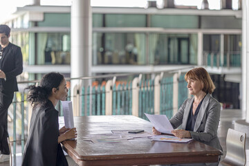 Conversation between a female senior manager with her young African coworker using data and diagram to design for a business development plan. Working across generations and cultures