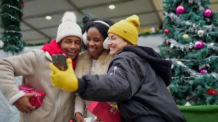 Cheerful multiethnic friends capturing memorable selfie moment at festive christmas market, wearing warm winter clothing and sharing joyful holiday experience - Powered by Adobe