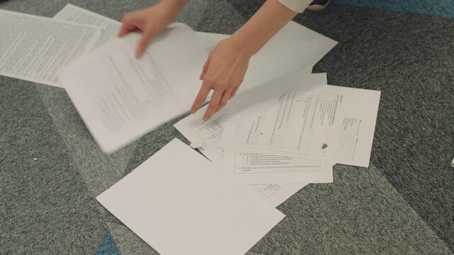 Young girl scattering important documents from floor. Young employee of office of prestigious company carefully collecting papers from floor.