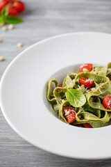 Homemade green tagliatelle pasta with pesto on a plate on the table. Italian cuisine