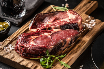 Dry aged ribeye steaks on wooden cutting board with arugula and sea salt