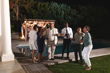 Group of diverse seniors celebrating by poolside, enjoying drinks and laughter