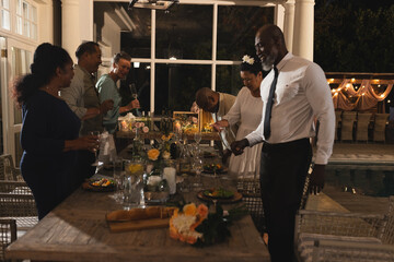 African American man celebrating with friends at elegant dinner party by poolside