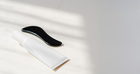 Gua sha tool and skincare product on a bathroom countertop with soft natural light streaming...