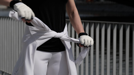 A woman s hands adjust a tied sweatshirt, emphasizing details of workout attire and fitness accessories. The growing focus on activewear reflects the fusion of fashion and functionality in modern
