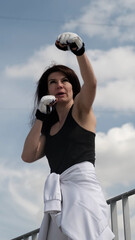 A fit woman in workout gloves performs a striking motion, her eyes locked on an unseen target. The popularity of combat training showcases the modern pursuit of self-defense and personal power.