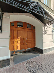 An elegant wooden door with decorative glass panels and geometric carvings, set in a pale facade. This image reflects timeless architectural style and refined urban aesthetic