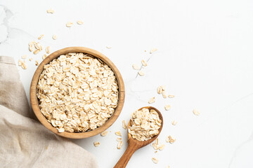 Rolled oats or oat flakes in a wooden bowl on white background. Top view with copy space.