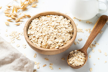 Rolled oats or oat flakes in a wooden bowl on white background.
