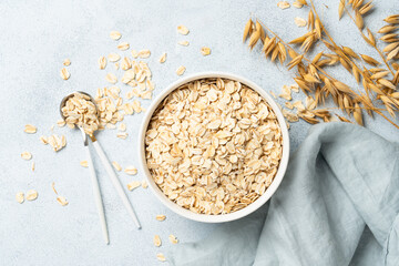 Rolled oats flakes in a wooden bowl with ears. Top view on white background.