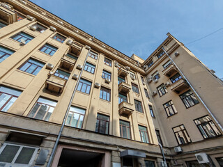A tall beige building with repeating windows, balconies, and visible air conditioning units. The image captures the practical design of urban residential spaces in densely populated areas.