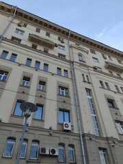 An urban apartment building featuring multiple small balconies, large windows, and air conditioning units on a light gray facade. The image emphasizes the simplicity of contemporary residential