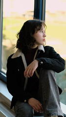 A contemplative girl sits by a window, her gaze directed outward. The photo highlights a reflective mood, symbolizing personal growth and the beauty of stillness.