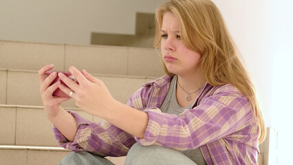A blonde girl in a plaid shirt furrows her brow while using her smartphone, reflecting the intensity of digital interactions. The scene underscores the challenges of modern connectivity.