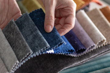 A hand touches a fabric sample book in a showroom or artisan upholstery workshop. Ideal for projects on interior design, furnishing, and material selection.