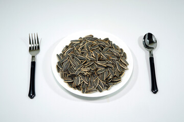 Roasted sunflower seeds on black plate with cutlery set together on white background close up view flat lay photography