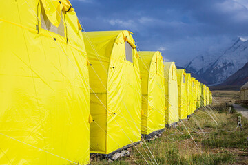 alpine camp with yellow tents in the base camp in front of the big peak of the mountain, preparation of climbers for the ascent to avoid the death of climbers without acclimatization