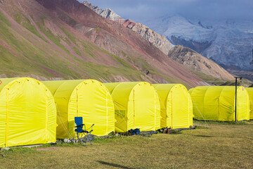 alpine camp with yellow tents in the base camp in front of the big peak of the mountain, preparation of climbers for the ascent to avoid the death of climbers without acclimatization