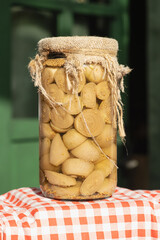 Close-up of a glass jar with pickled onions covered in burlap, standing on a red checkered cloth at a local farmers market