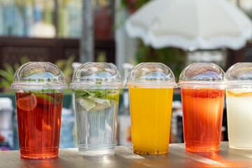 Row of assorted refreshing beverages in plastic cups with dome lids, displayed on a wooden surface at a summer street cafe or outdoor market