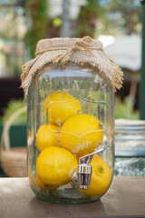 Transparent glass jar with fresh lemons and metal tap, covered with burlap cloth, styled as eco-friendly decor for outdoor summer event