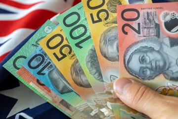 New Australian dollars held in hand against the Australian flag. Financial and economic concept....