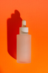Frosted glass serum bottle with white dropper on vibrant orange background, minimal design
