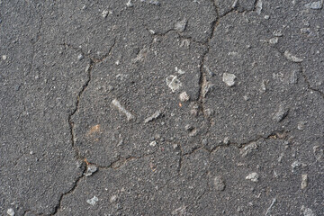 Close-up of cracked asphalt texture with rough surface and small stones, natural urban background.