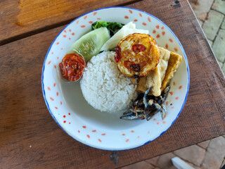 Tempong rice, Tempong rice is equipped with fresh vegetables, salted fish, eggs, chili sauce, tempeh, tofu and other accompaniments. Tempong rice is a typical food from Banyuwangi, Indonesia.