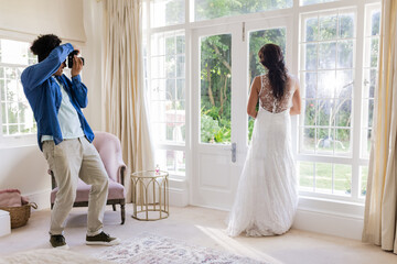 Photographer capturing bride in elegant gown standing by large window