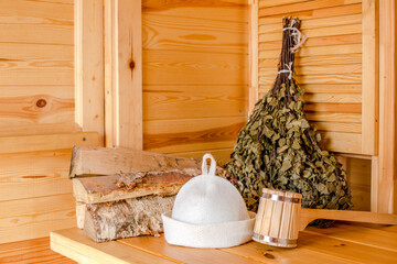 Various sauna accessories in a wooden Finnish sauna or Russian bathhouse with traditional sauna accessories: birch broom, felt hat,pumice, birch wood medicinal herbs. Relax concept. Copy space