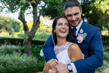 Bride and groom embracing joyfully in lush garden, celebrating their wedding day