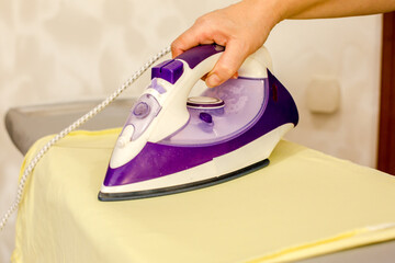 Close up young woman hand use electric steam, hot iron press pile stripe shirt clothes on ironing board, housework after hygiene laundry at home. Housekeeping lifestyle, household of chores concept.