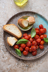Plate with ciabatta, roasted cherry tomatoes and fresh basil, vertical shot on a beige granite background, elevated view