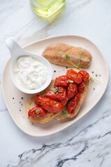 Stracciatella cheese and roasted tomato bruschettas on a beige plate, vertical shot on a white stone background, elevated view