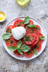 Tomato salad with basil oil and buffalo mozzarella, vertical shot on a light-brown granite background, elevated view