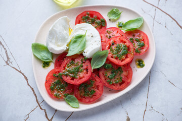 Sliced red tomatoes with basil oil and torn buffalo mozzarella, horizontal shot on a white granite background, elevated view
